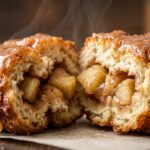 Ultra close-up macro of a warm golden-brown deep-fried bakery apple fritter broken gently in half revealing spiced apple chunks and cider glaze