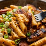 Ultra close-up macro of ridged penne pasta tossed with sliced spiced halal sausage and blackened chicken in creamy Cajun Parmesan sauce