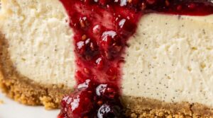 Ultra close-up macro of a slice of decadent New York vanilla bean cheesecake with buttery graham crust and glistening ruby berry compote