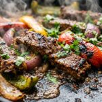 Ultra close-up macro of sizzling caramelized halal flank steak strips nestled among blistered charred bell peppers and red onions on a sheet pan