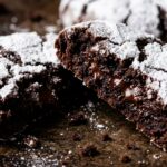 Ultra close-up macro of fudgy chocolate crinkle cookie broken in half showing molten brownie center and snowy powdered sugar cracks