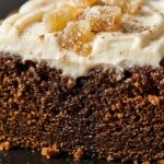 Ultra close-up macro of a slice of moist spiced dark gingerbread loaf cake with thick velvety cream cheese frosting swirl and candied ginger