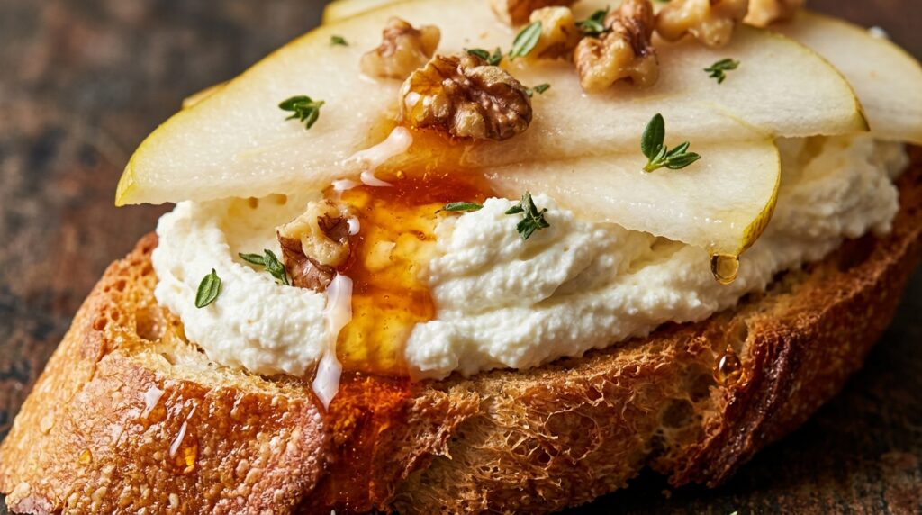 Ultra close-up macro of crispy toasted crostini topped with fluffy whipped ricotta, sliced pears, toasted walnuts, and spicy hot honey drizzle