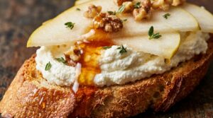 Ultra close-up macro of crispy toasted crostini topped with fluffy whipped ricotta, sliced pears, toasted walnuts, and spicy hot honey drizzle