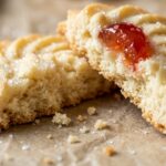 Ultra close-up macro of melt-in-your-mouth whipped shortbread cookie split in half showing delicate crumbly texture and candied cherry